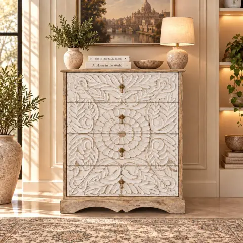 Hand-carved floral four-drawer chest of drawers in distressed white finish with brass-tone drop handles, shown closed in a warm interior setting.