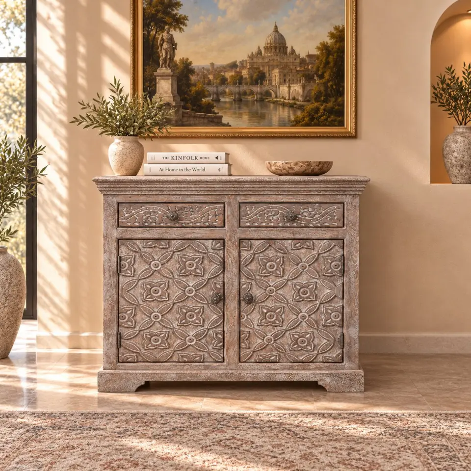 Hand-carved mango wood storage cabinet with two floral-patterned doors, two upper drawers, antique-style knobs and a distressed whitewashed finish in a warm interior setting.