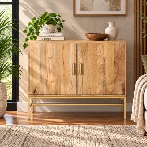 Two door natural wood cabinet shown closed in a warm interior with visible grain variation, vertical metal handles and a brass-tone raised base.